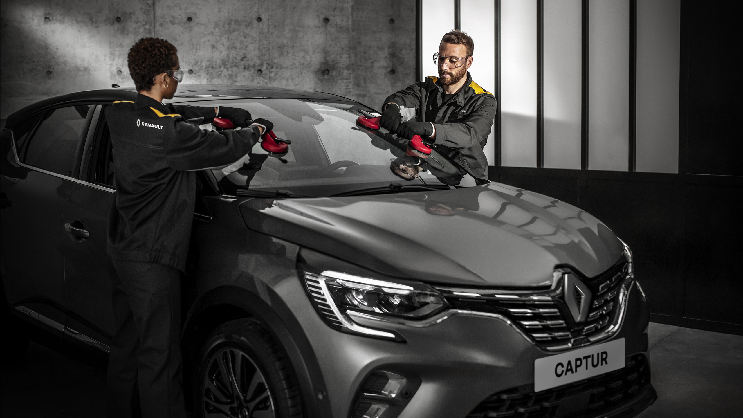 Du serviso technikai keičia pilko Renault automobilio priekinį stiklą.