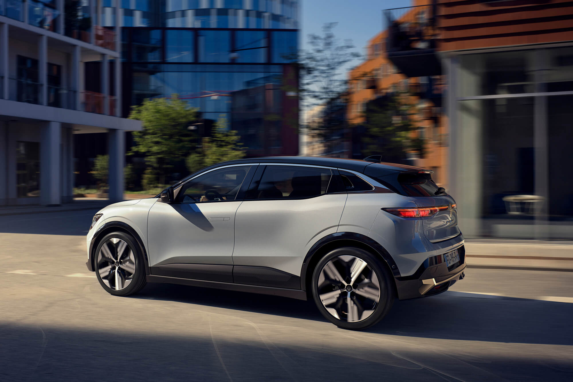 Pilkas visiškai elektrinis Renault MEGANE E-TECH Electric dinamiškai važiuoja mieste