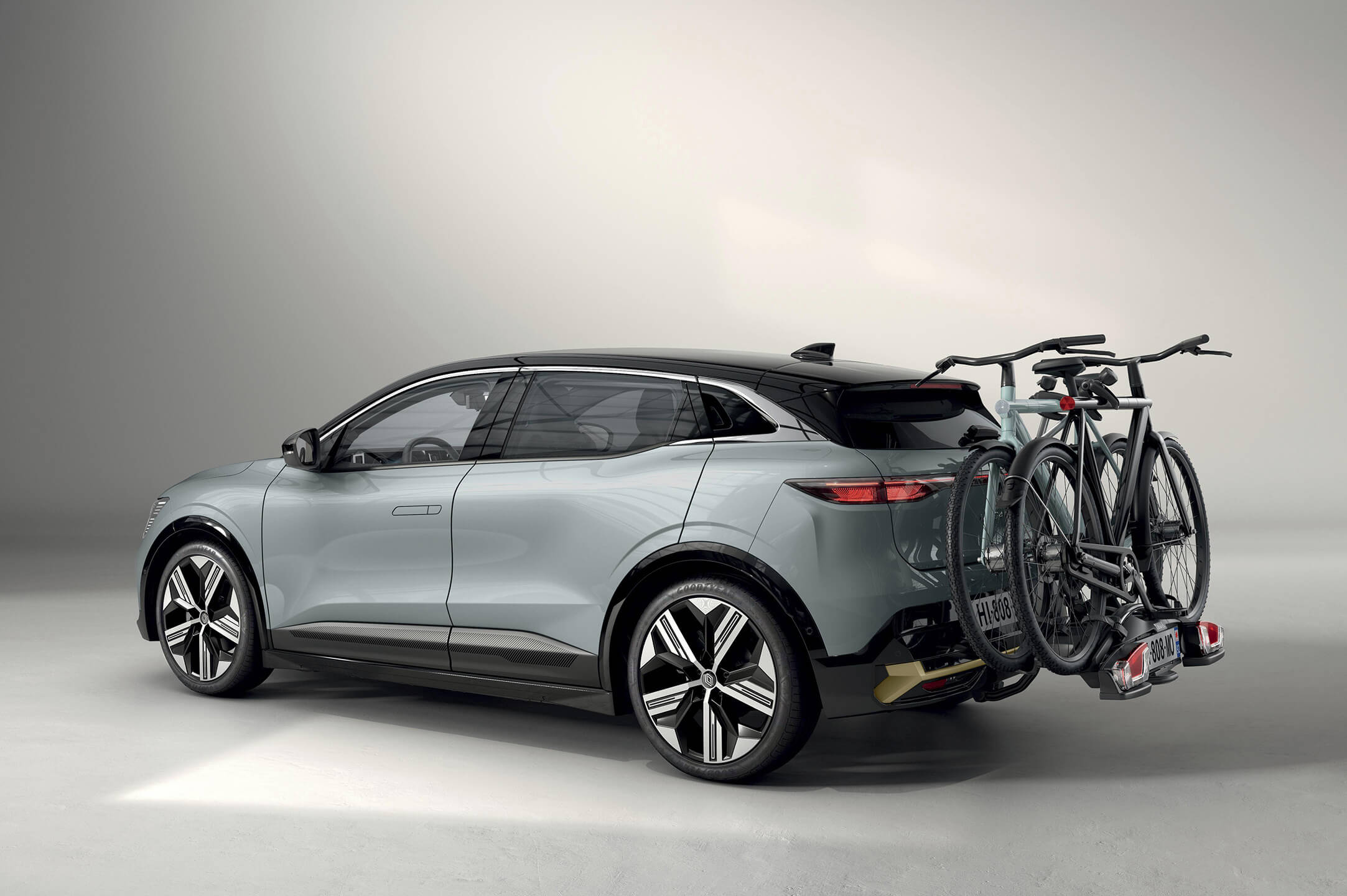 Pilkas visiškai elektrinis Renault MEGANE E-TECH Electric su prie vilkimo kablio pritvirtintu dviračių laikikliu studijos fone, matomas iš šono