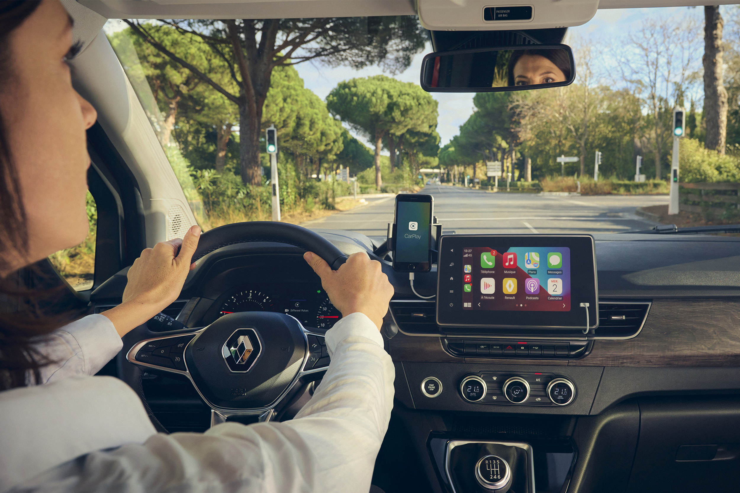 Moteris, laikanti rankas ant Renault KANGOO vairo, žiūri į galinio vaizdo veidrodėlį
