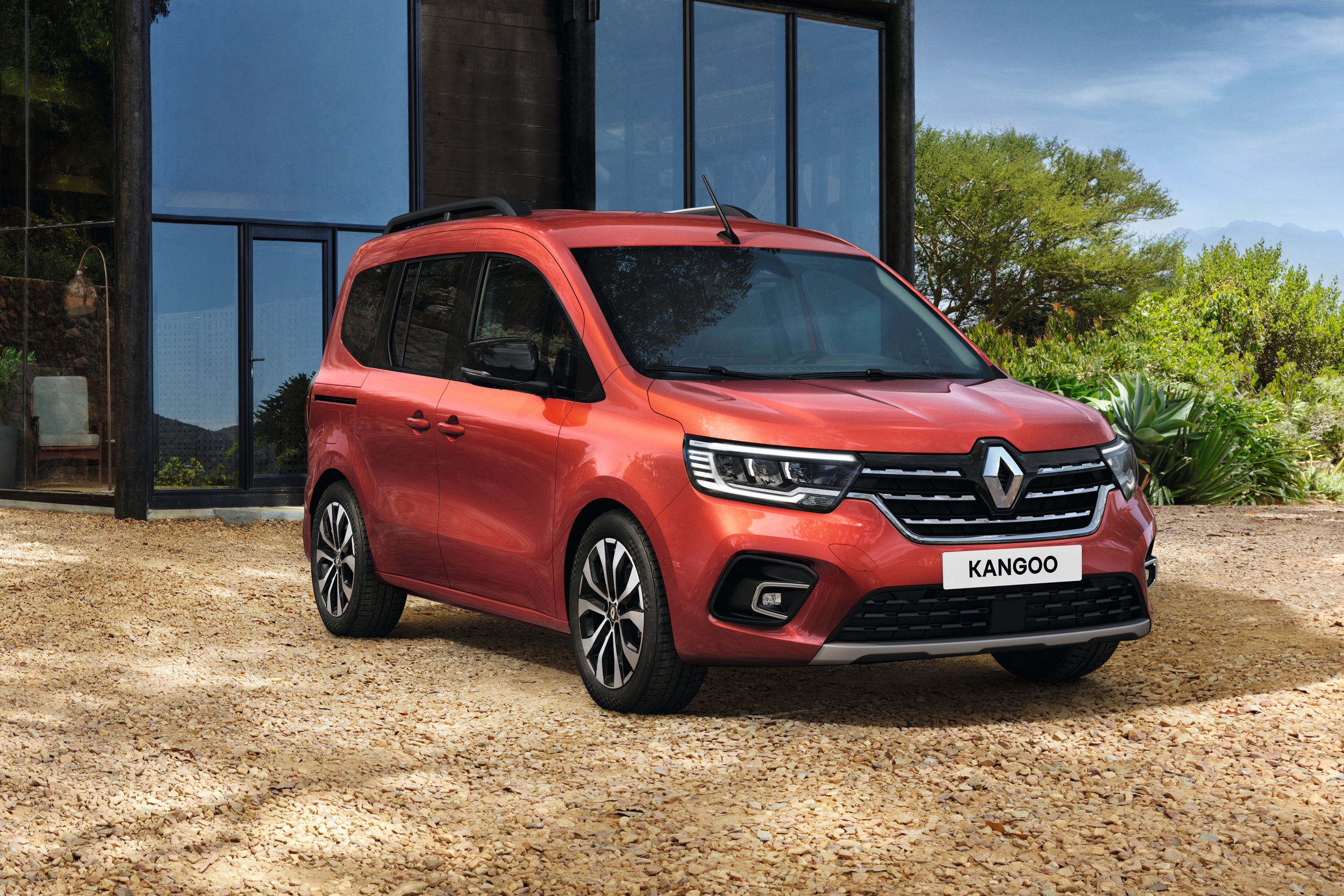 Terracotta Brown rudos spalvos Renault KANGOO vienatūris, pastatytas ant smulkios skaldos dangos priešais tamsų pastatą