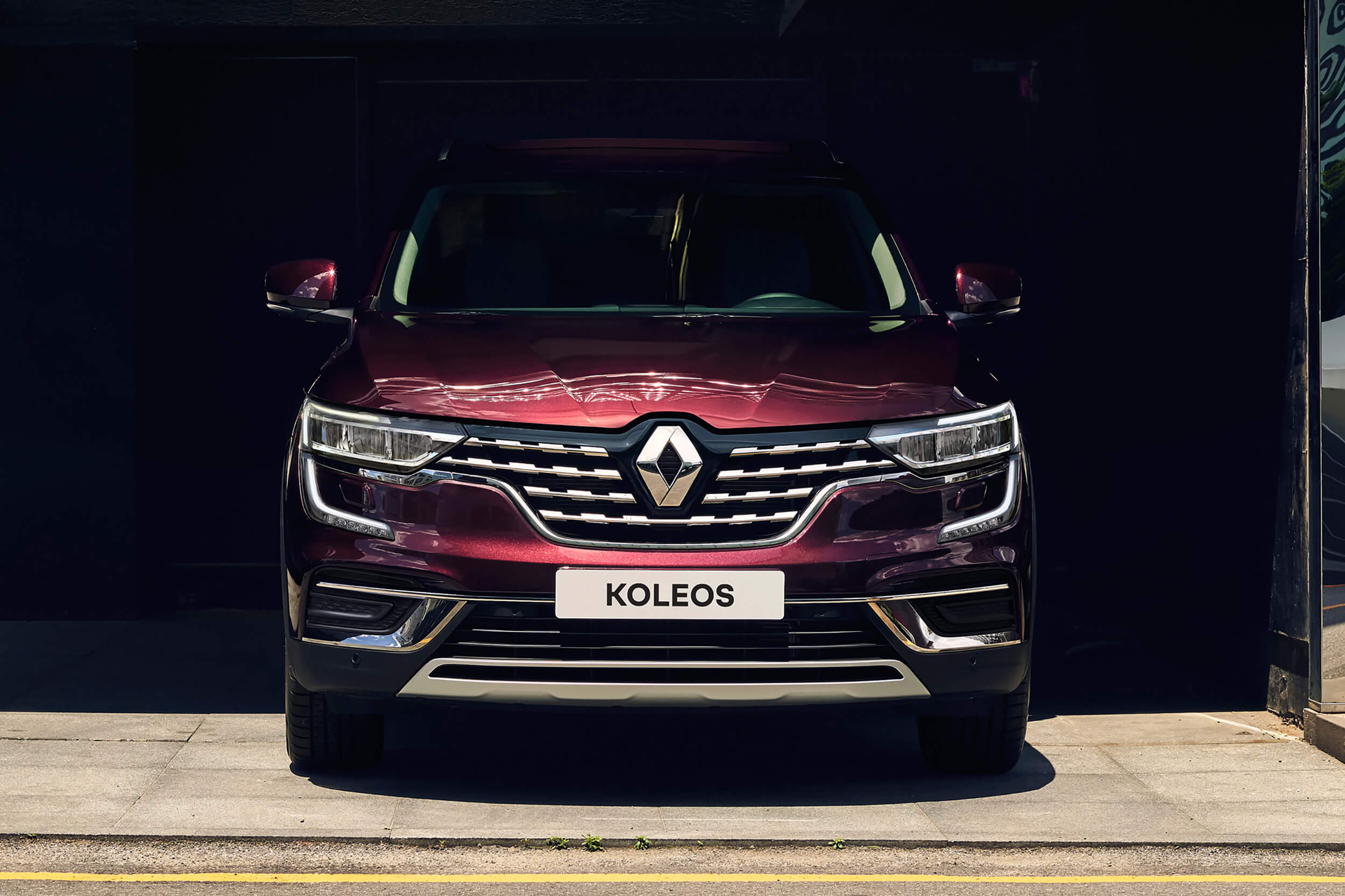 Tamsiai raudonos spalvos visureigio Renault Koleos, stovinčio pastogėje, priekinė dalis