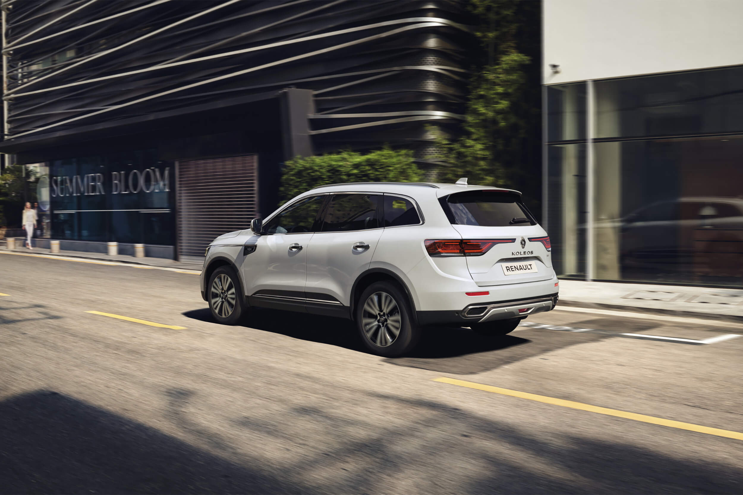 Baltas visureigis Renault Koleos važiuoja miesto gatve, matomas iš galinės pusės