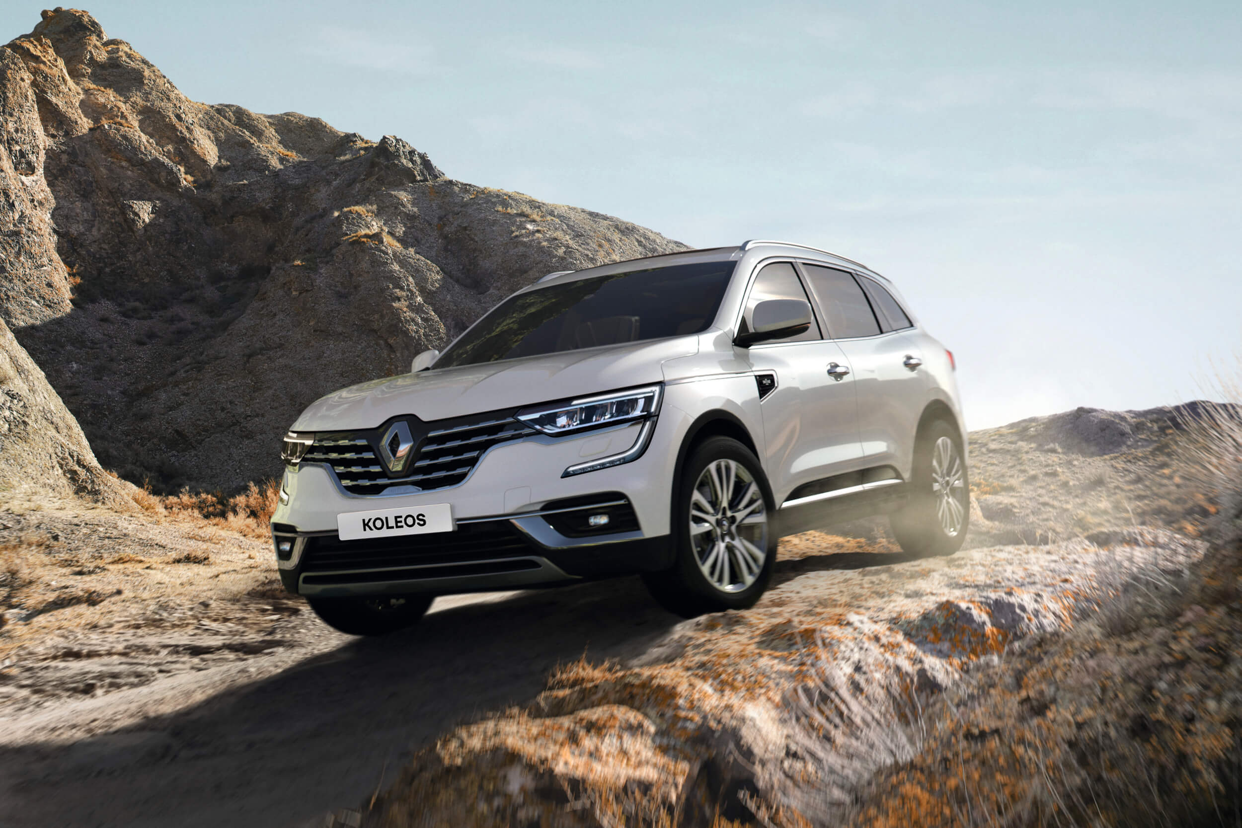 Baltas Renault Koleos visureigis važiuoja žemyn nuo kalno uolėtu keliu